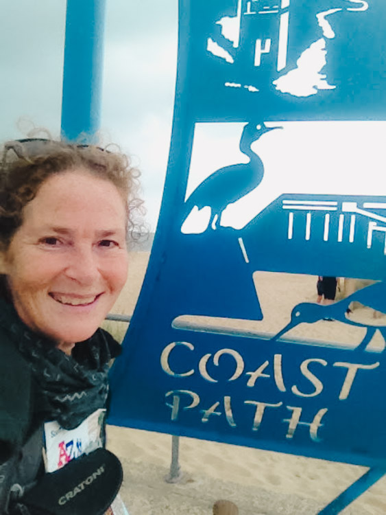 Smiling beside the blue metal sculpture at the end of the South West Coast PAth