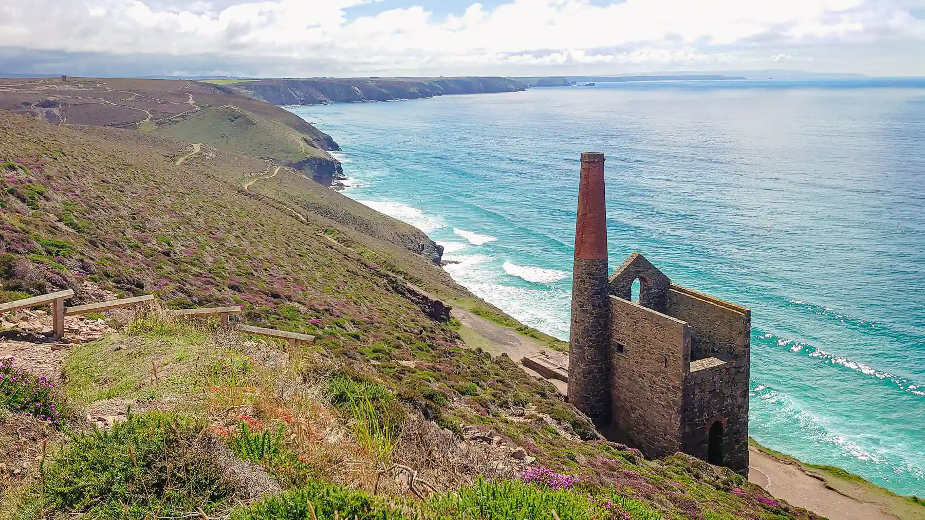 On the edge of the cliff, the ruin of an old engine house stands out against the crystal clear sea