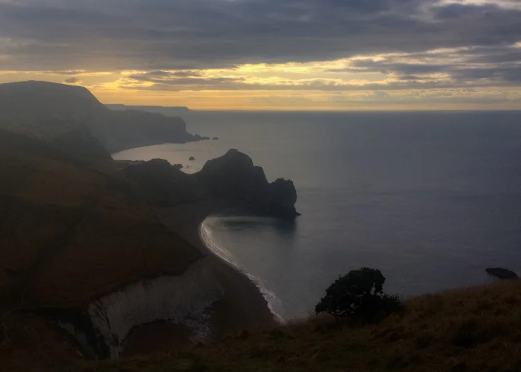 Durdle Door rocks in silhouette against a golden sunrise