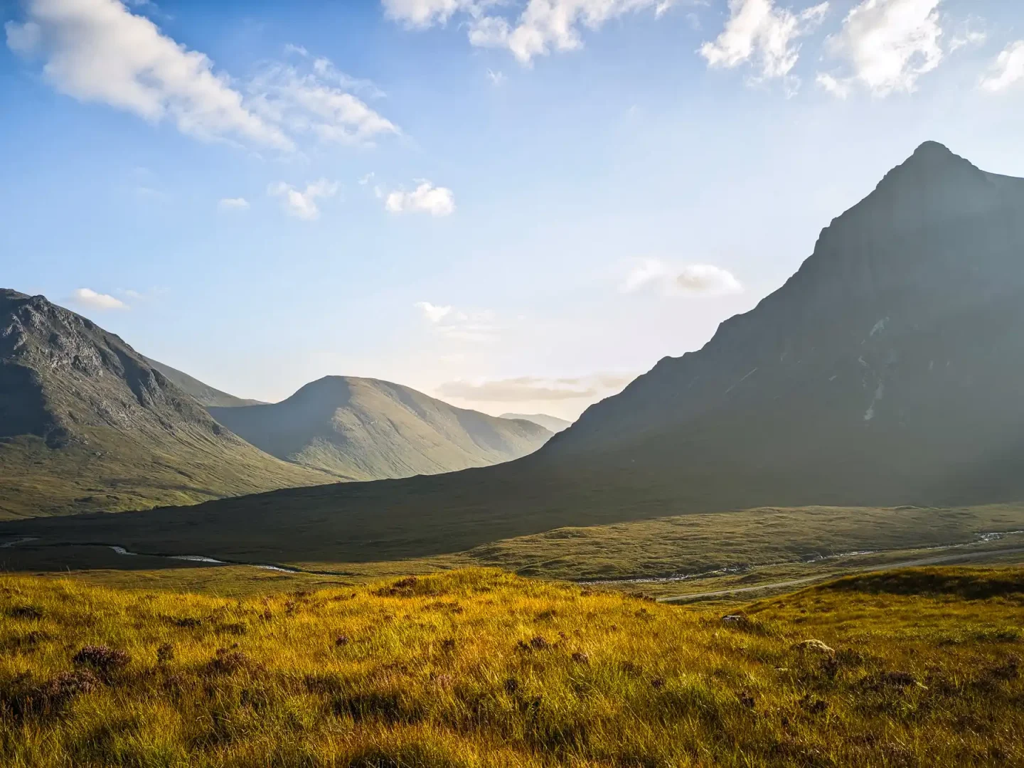 A sharp triangular-shaped mountain rises steeply on the right in the foreground, with softer more rounded mountains on the left. It's a bright, sunny end to the day.