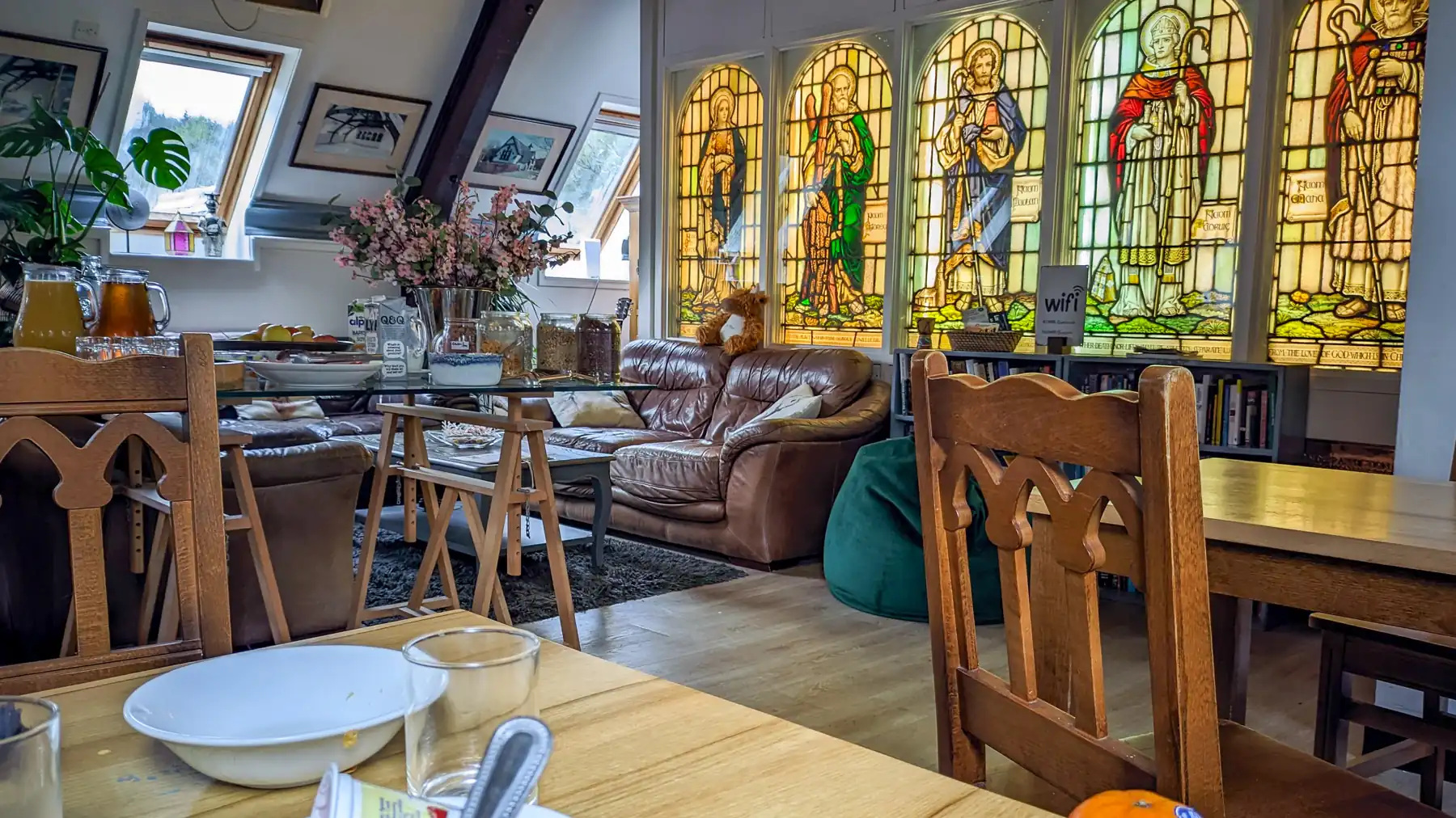 Tables laid for breakfast in a hostel. Comfy sofas and a stained glass screen give the space a homely feel.
