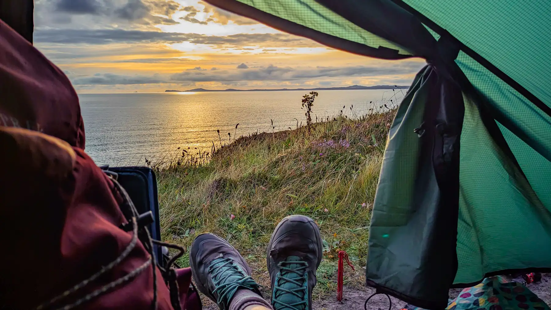 A walker, sitting in her tent, looks out at a peaceful sunset over the sea. 