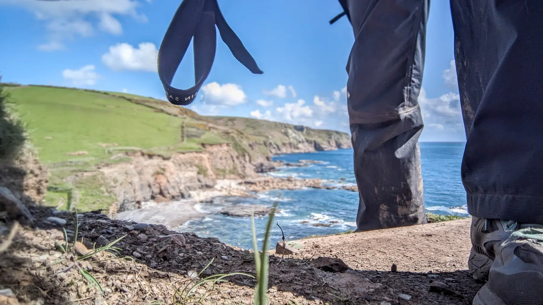 A hiker walks along a cliff path and this is a low down view with a detail of her legs and cliff path behind.