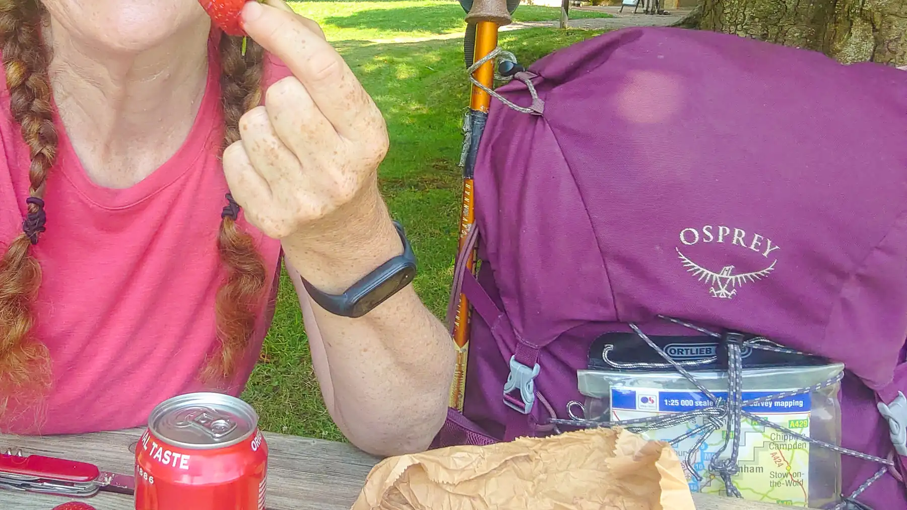 Close up. Sitting at a picnic bench with my Osprey backpacking rucksack beside me, fully packed and with a map strapped to the outside. On the table, there's a can of coke and a Swiss army knife.