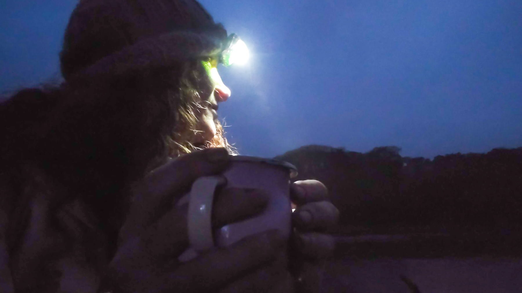 It's dark and I'm sitting on the ground with a head-torch on drinking from an enamel mug. There's a hazy shadow of trees behind me.