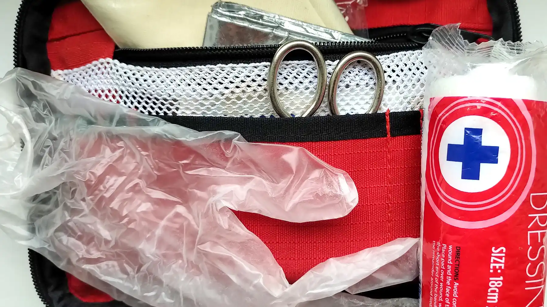 A large, red first aid kit opened with a dressing, glove and scissors on view.