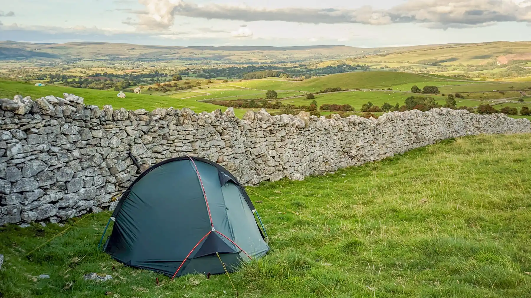 My tent set up beside a drystone wall at dusk, with rolling hills and moorland behind.